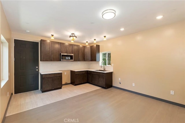 kitchen featuring stainless steel microwave, baseboards, dark brown cabinetry, light wood-style flooring, and a sink