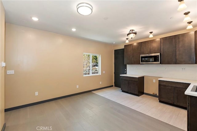 kitchen with stainless steel microwave, dark brown cabinets, baseboards, light countertops, and light wood-style floors