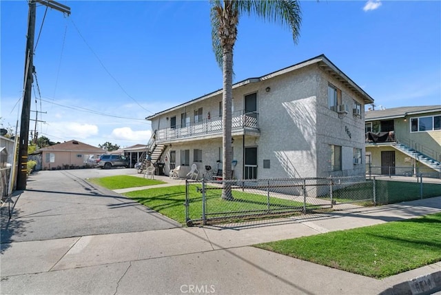 view of front property featuring a front lawn, a balcony, a fenced front yard, and stucco siding