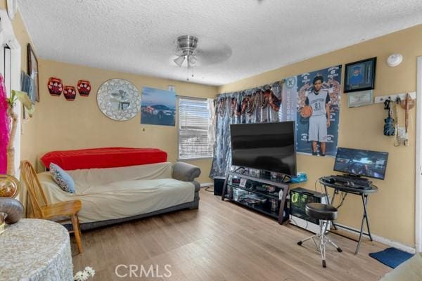 living room with ceiling fan, wood finished floors, baseboards, and a textured ceiling