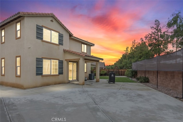 back of house at dusk with central AC unit, fence, stucco siding, a tile roof, and a patio area