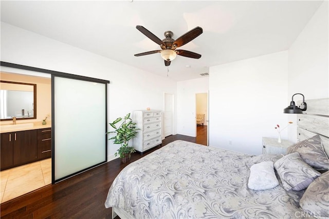 bedroom with visible vents, a sink, ensuite bath, wood finished floors, and ceiling fan