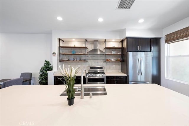 kitchen featuring open shelves, wall chimney range hood, light countertops, stainless steel appliances, and a sink