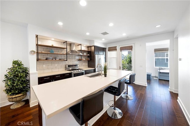 kitchen featuring a sink, stainless steel appliances, dark wood finished floors, and wall chimney range hood