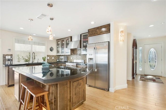 kitchen featuring visible vents, backsplash, stainless steel appliances, wall chimney exhaust hood, and light wood finished floors