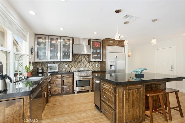 kitchen featuring visible vents, high quality appliances, tasteful backsplash, a breakfast bar area, and wall chimney range hood