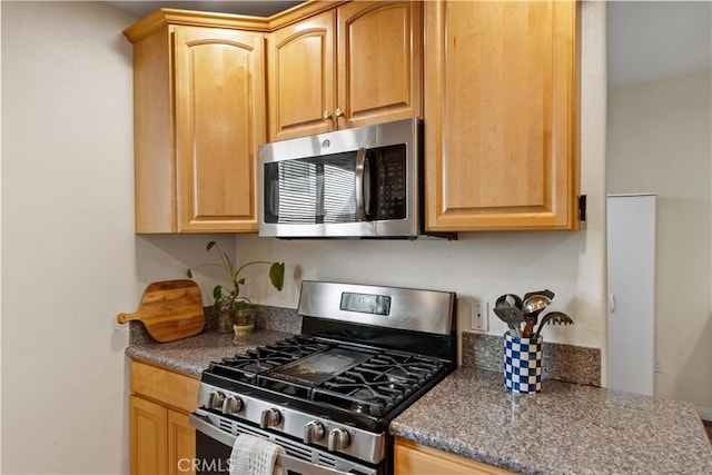 kitchen with stainless steel appliances, dark countertops, and light brown cabinetry