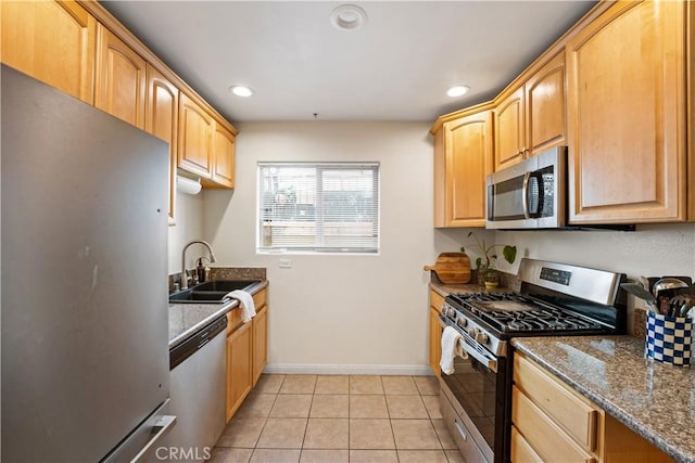 kitchen with dark stone countertops, light tile patterned floors, light brown cabinets, a sink, and appliances with stainless steel finishes