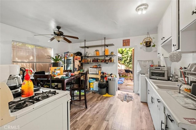 kitchen with light wood finished floors, white range with gas stovetop, light countertops, white cabinets, and stainless steel microwave