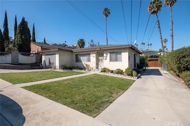 view of front of home with concrete driveway, fence, a front lawn, and stucco siding