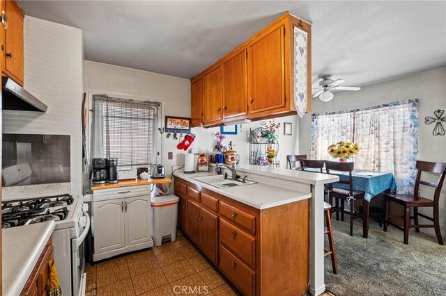 kitchen with a peninsula, white range with gas stovetop, light countertops, and a sink