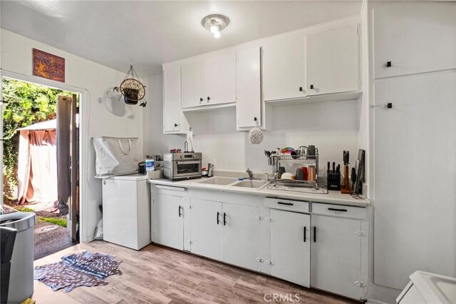 kitchen with light wood-style flooring, a toaster, a sink, light countertops, and white cabinetry