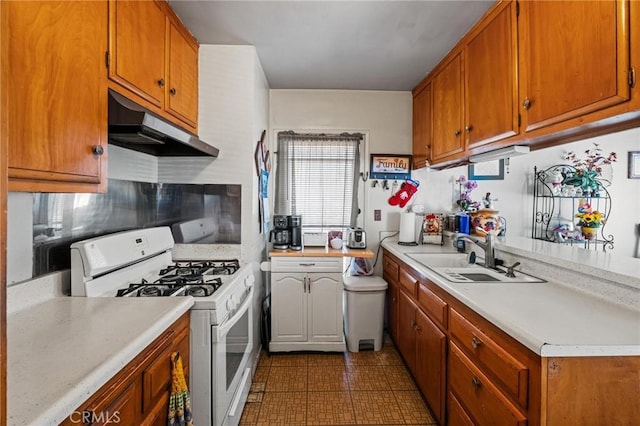 kitchen featuring under cabinet range hood, light countertops, white gas range, brown cabinets, and a sink