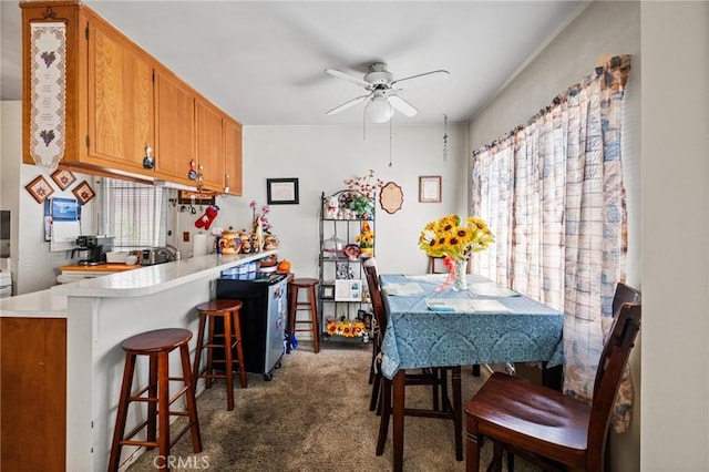 kitchen featuring brown cabinetry, a breakfast bar, a peninsula, light countertops, and dark carpet