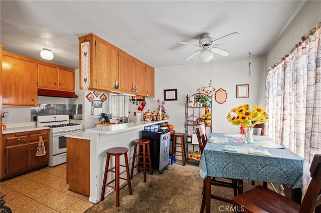 kitchen featuring white range with gas cooktop, a peninsula, ceiling fan, light countertops, and a kitchen breakfast bar