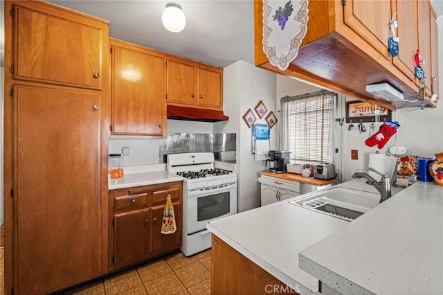 kitchen featuring white gas stove, light countertops, under cabinet range hood, and a sink