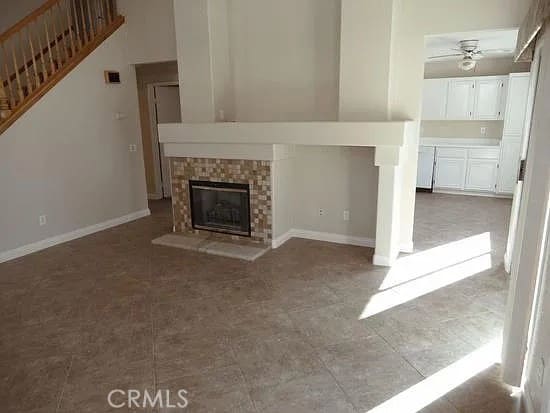 unfurnished living room featuring visible vents, baseboards, ceiling fan, stairway, and a glass covered fireplace