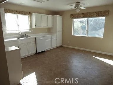 kitchen with a ceiling fan, a sink, white cabinetry, white dishwasher, and baseboards