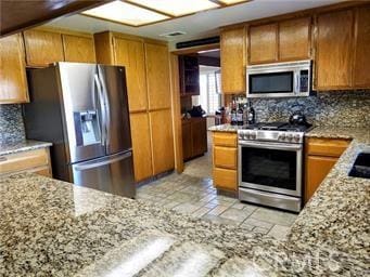 kitchen featuring backsplash, brown cabinets, stainless steel appliances, and light stone countertops