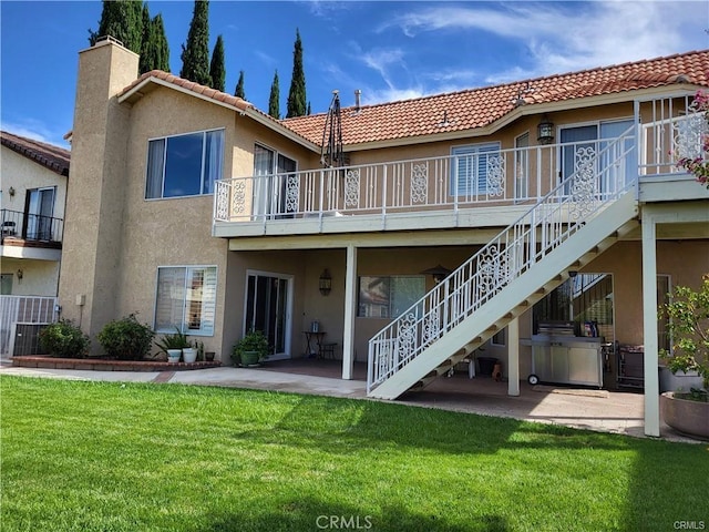 back of house with a yard, a chimney, stairs, stucco siding, and a patio area