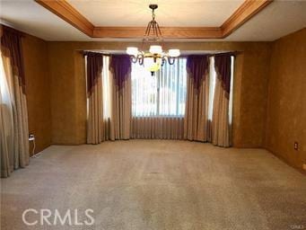 carpeted spare room with a raised ceiling, a chandelier, and ornamental molding