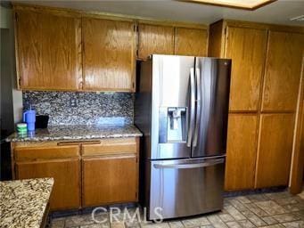 kitchen with stainless steel fridge, tasteful backsplash, brown cabinetry, and light stone countertops