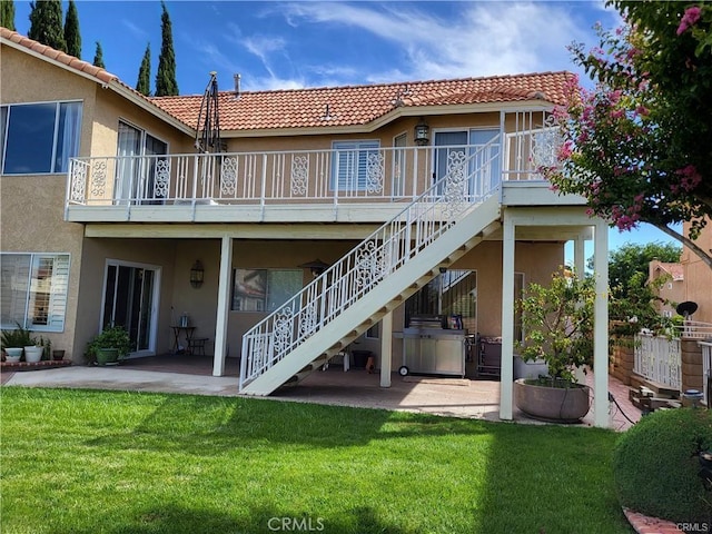 rear view of house with a tiled roof, stairs, stucco siding, a yard, and a patio area