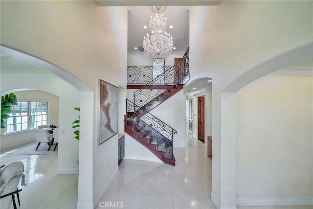 tiled entryway with baseboards, arched walkways, stairs, a towering ceiling, and a chandelier