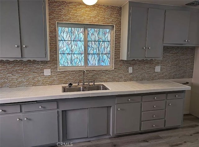 kitchen featuring backsplash, visible vents, gray cabinets, and a sink