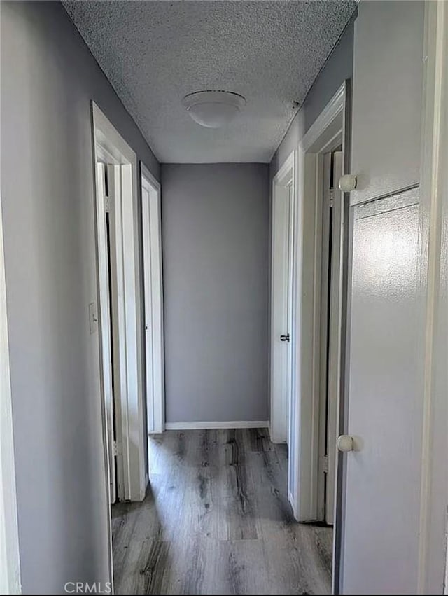 corridor featuring baseboards, a textured ceiling, wood finished floors, and plenty of natural light