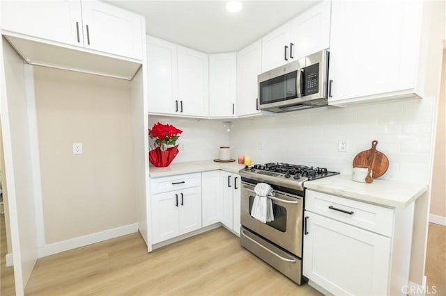 kitchen with baseboards, light wood finished floors, white cabinets, appliances with stainless steel finishes, and backsplash