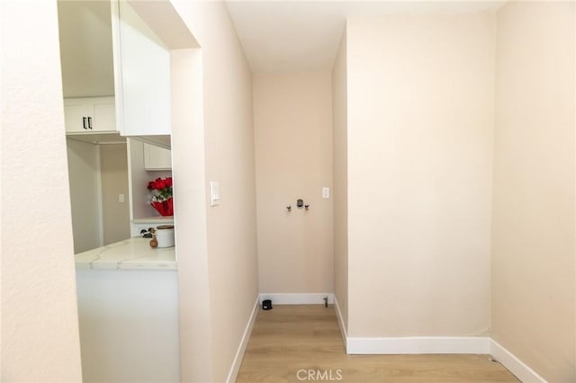 clothes washing area featuring baseboards and light wood-type flooring