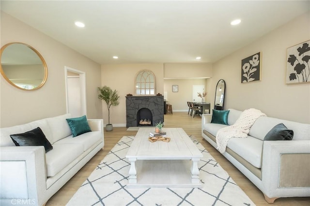 living room featuring recessed lighting, a fireplace, baseboards, and light wood-style floors