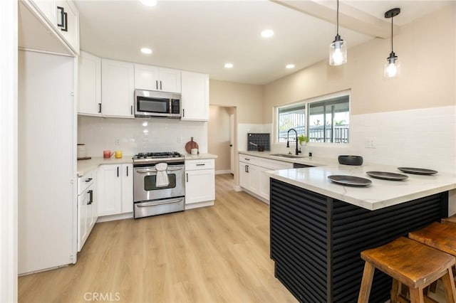 kitchen featuring light wood finished floors, a peninsula, appliances with stainless steel finishes, white cabinetry, and a kitchen breakfast bar