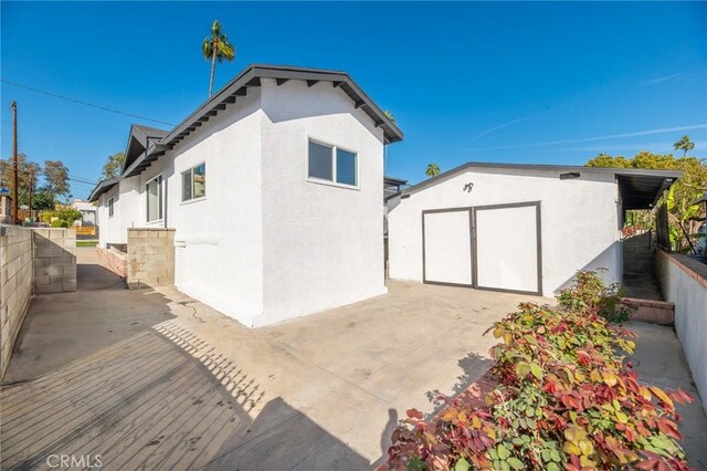 view of side of home featuring fence, stucco siding, a garage, an outdoor structure, and a patio area