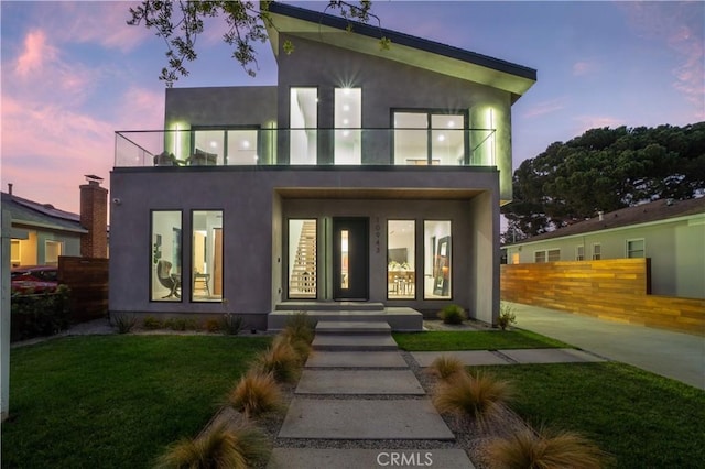 rear view of house featuring stucco siding, a balcony, and fence