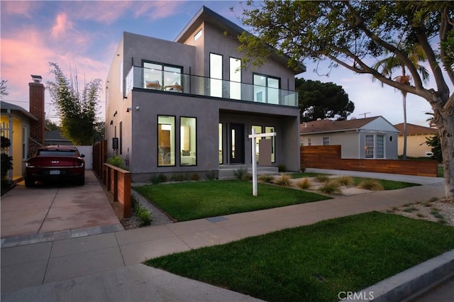 contemporary home with a balcony, a yard, fence, and stucco siding