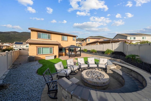 rear view of property featuring stucco siding, a fenced backyard, a fire pit, solar panels, and a patio area