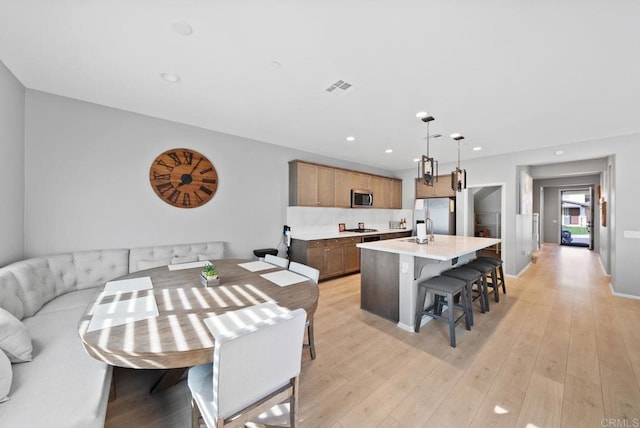 interior space featuring visible vents, an island with sink, light wood-style flooring, appliances with stainless steel finishes, and light countertops