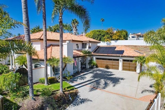 mediterranean / spanish home with solar panels, fence, a tile roof, an attached garage, and a gate