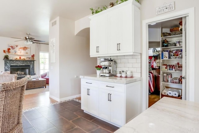 kitchen featuring visible vents, light stone counters, tasteful backsplash, a premium fireplace, and ceiling fan