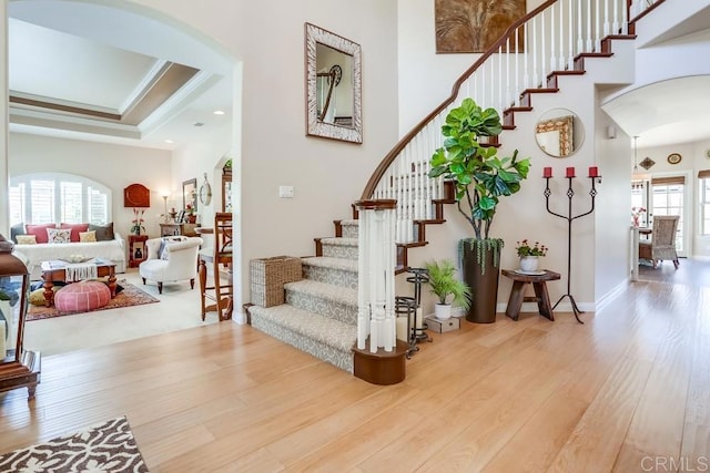 interior space featuring ornamental molding, wood finished floors, arched walkways, baseboards, and a towering ceiling