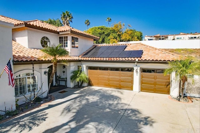 mediterranean / spanish house featuring solar panels, concrete driveway, a tile roof, stucco siding, and an attached garage