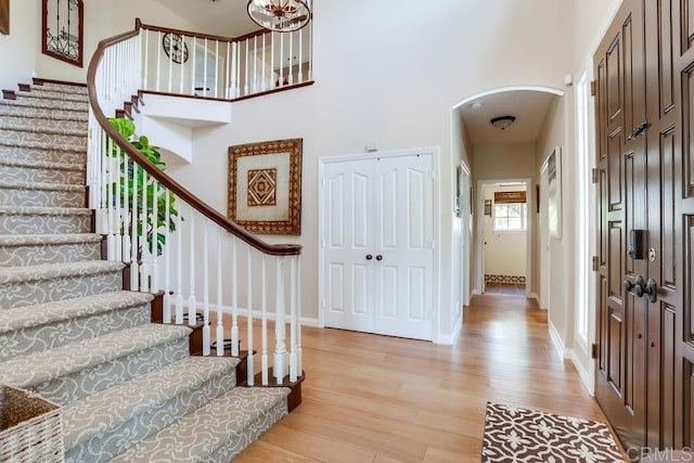 entrance foyer featuring baseboards, stairway, light wood-type flooring, a high ceiling, and arched walkways