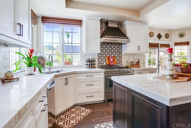 kitchen featuring light stone counters, stainless steel appliances, wall chimney exhaust hood, and a sink