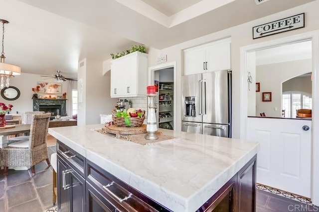 kitchen with light stone counters, a fireplace, high end refrigerator, white cabinetry, and backsplash