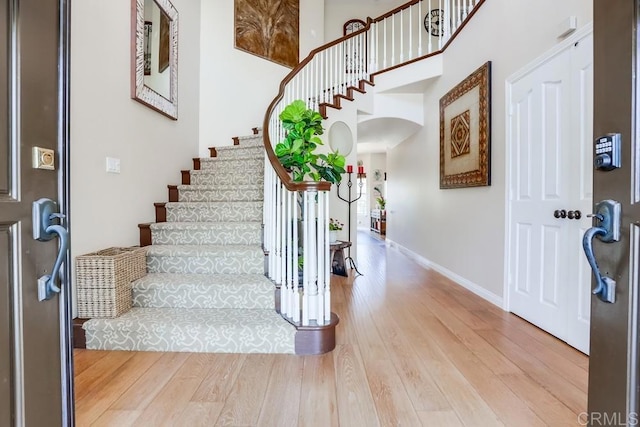 foyer entrance featuring stairway, baseboards, a high ceiling, and light wood-style floors