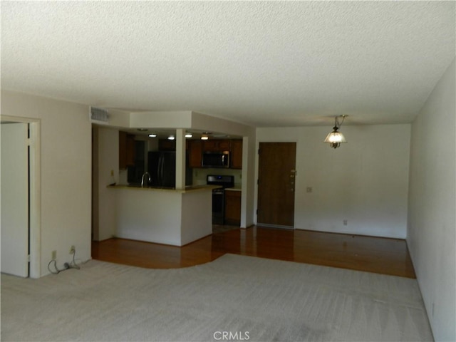 interior space featuring visible vents, black appliances, a textured ceiling, open floor plan, and a peninsula