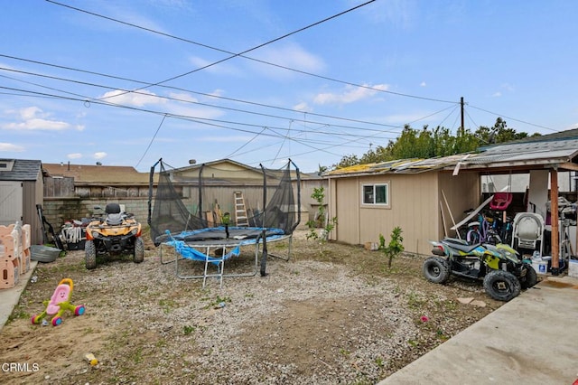 view of yard with an outbuilding, a trampoline, and fence