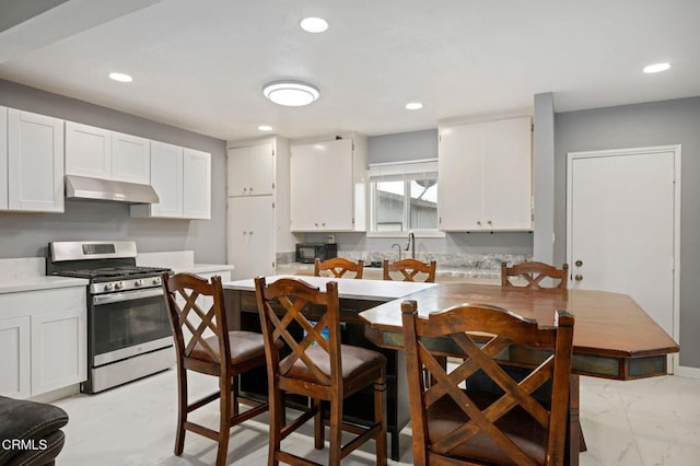 kitchen featuring black microwave, under cabinet range hood, stainless steel range with gas stovetop, white cabinets, and marble finish floor